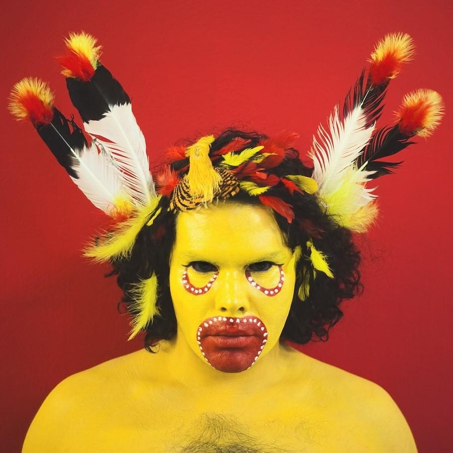 Man painted in yellow paint with feathers in his hair