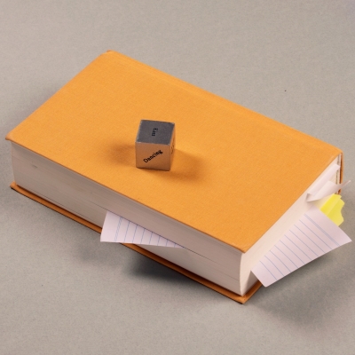 An image of a orange book with a game dice on top that features cryptic words. 
