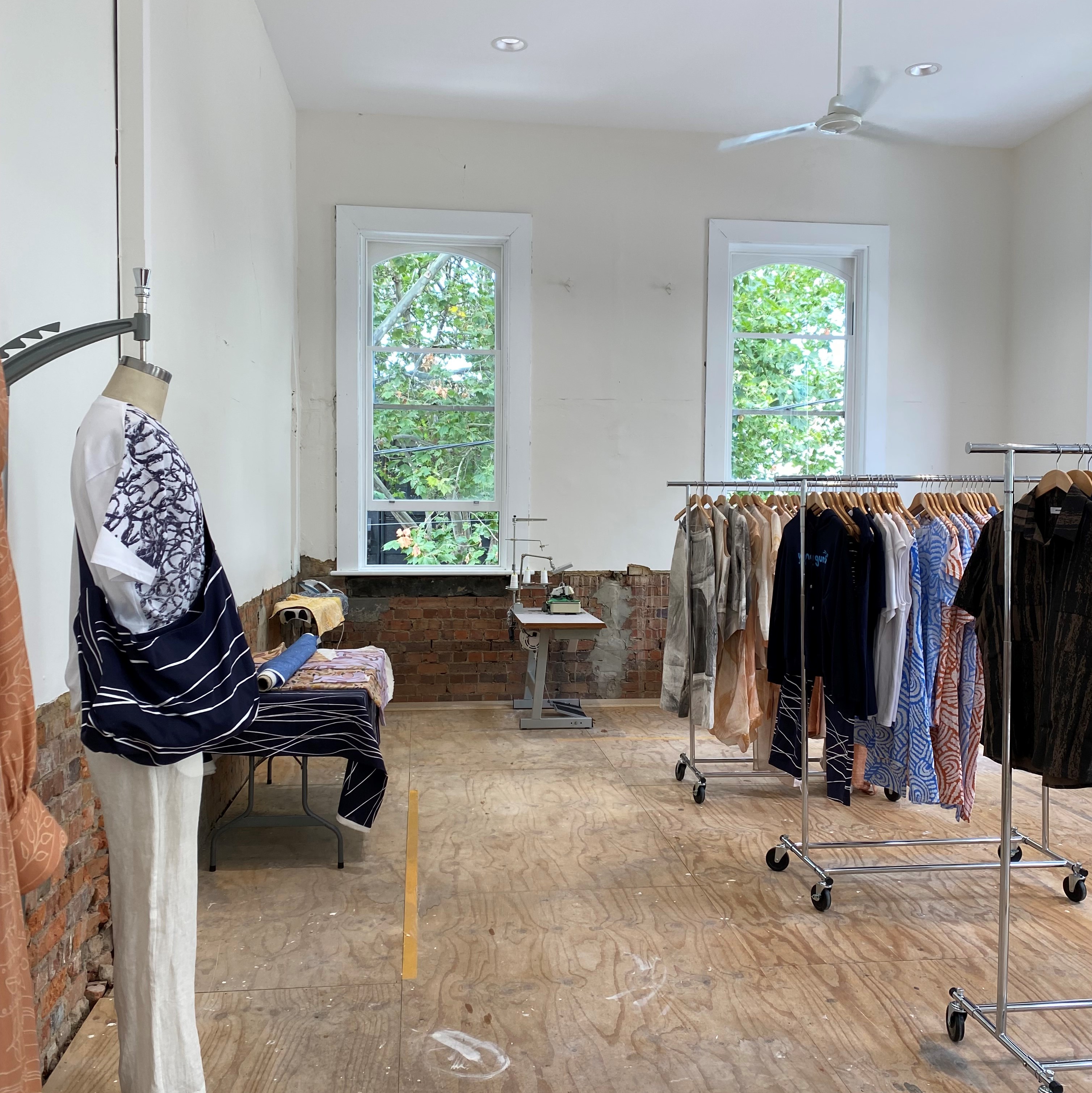 An interior view of the KIN Fashion studio, with racks of clothing and a mannequin sporting a top and bag. 