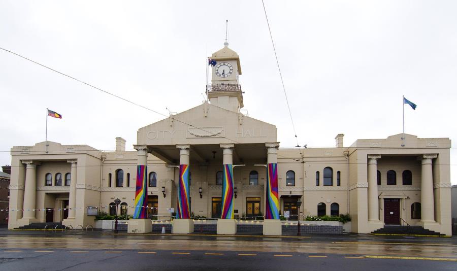 A photo of the Richmond Town Hall with it's 4 columns wrapped in colourful artworks banners