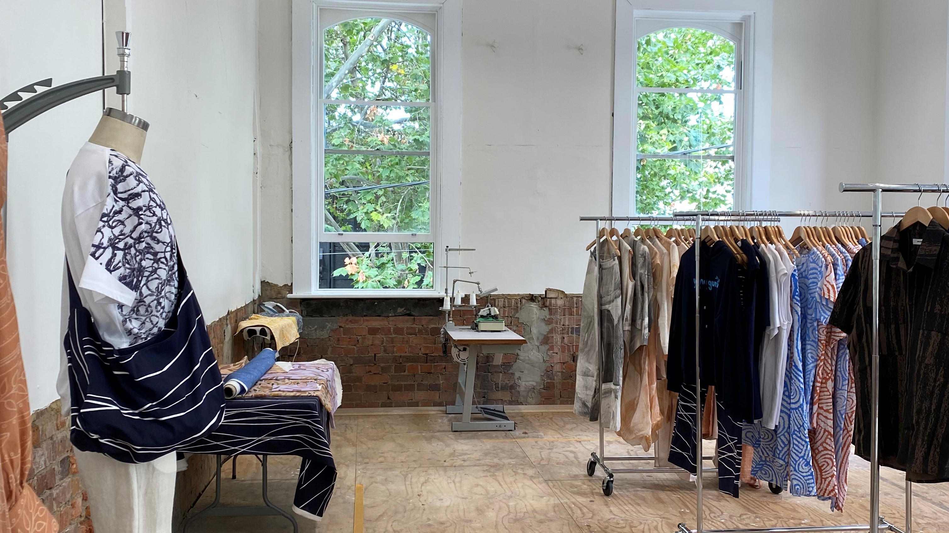 An interior view of the Kin Fashion studio, with racks of clothing and a mannequin sporting a top and bag. 