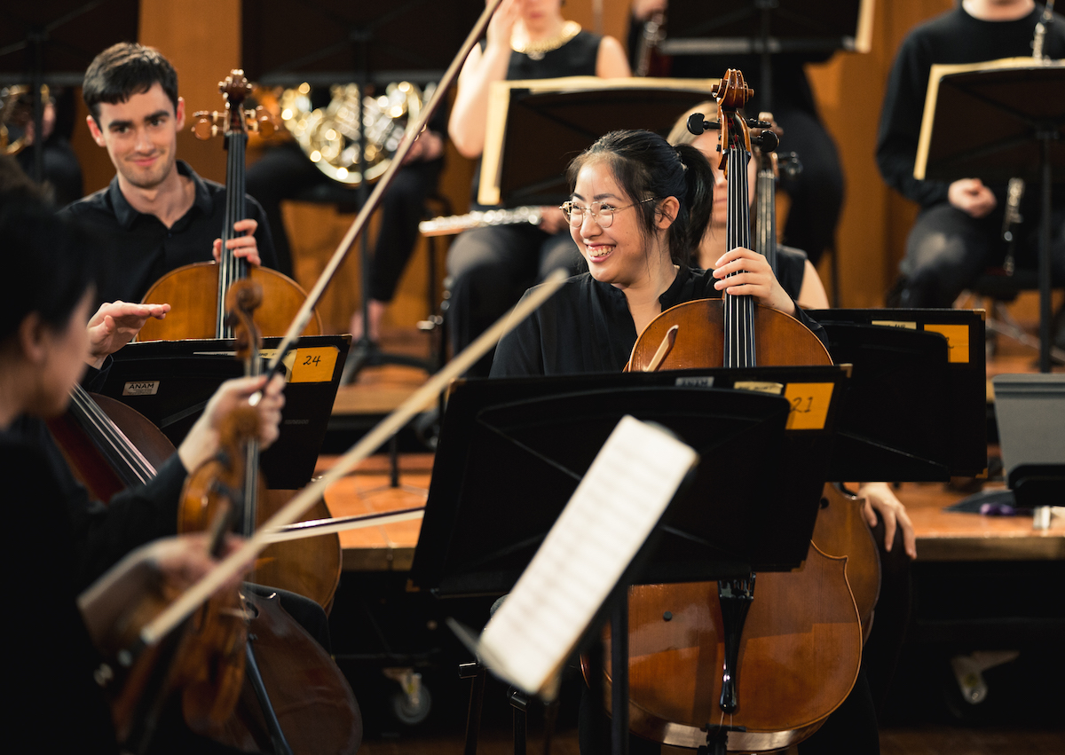 Two people playing orchestral instruments including a double bass with smiles on their faces
