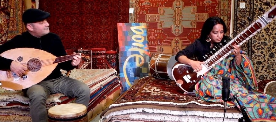 Musician Sarita McHarg and Yuval Ashkar sitting in a rug shop playing music.