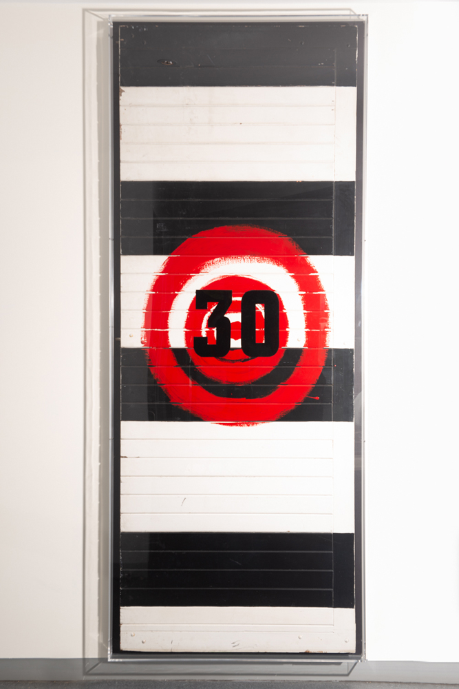 The artwork is made from the original doors located at the front entrance of the Collingwood Football Club’s grounds at Victoria Park.  The work depicts a big red target painted on the existing Blak and white stripes—Collingwood colours—of the door. Naina placed a fabric number ‘30’ on top of the target—created from material used for numbers on the back of players’ football vests. 