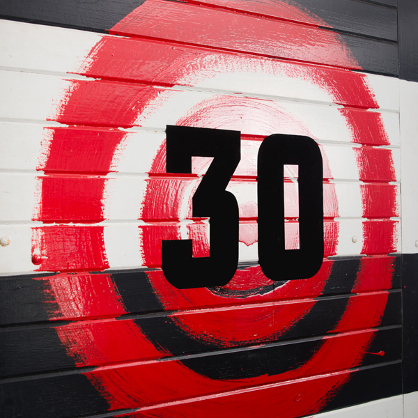 The artwork is made from the original doors located at the front entrance of the Collingwood Football Club’s grounds at Victoria Park. The work depicts a big red target painted on the existing Blak and white stripes—Collingwood colours—of the door. Naina placed a fabric number ‘30’ on top of the target—created from material used for numbers on the back of players’ football vests. 