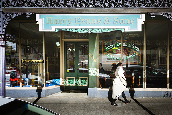 Person in white coat walking past Harry Evans and Sons shopfront