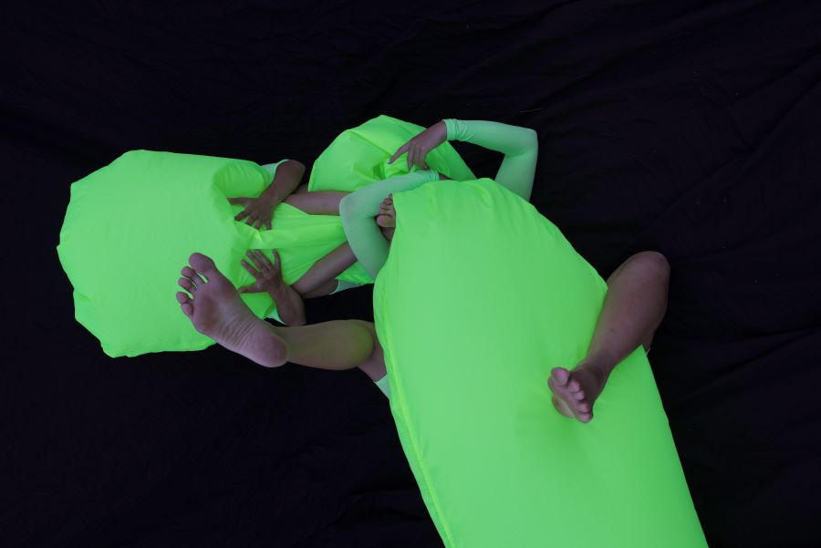 2 people with a green sheet covering them and only arms and legs can be seen from their bodies