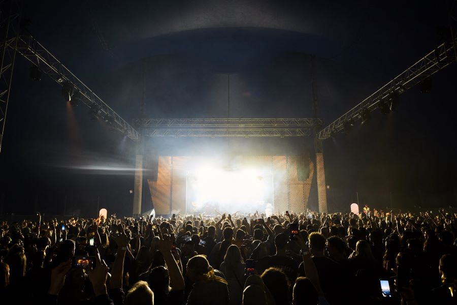 A stage with bright lights shining out over a crowd under a festival tent.