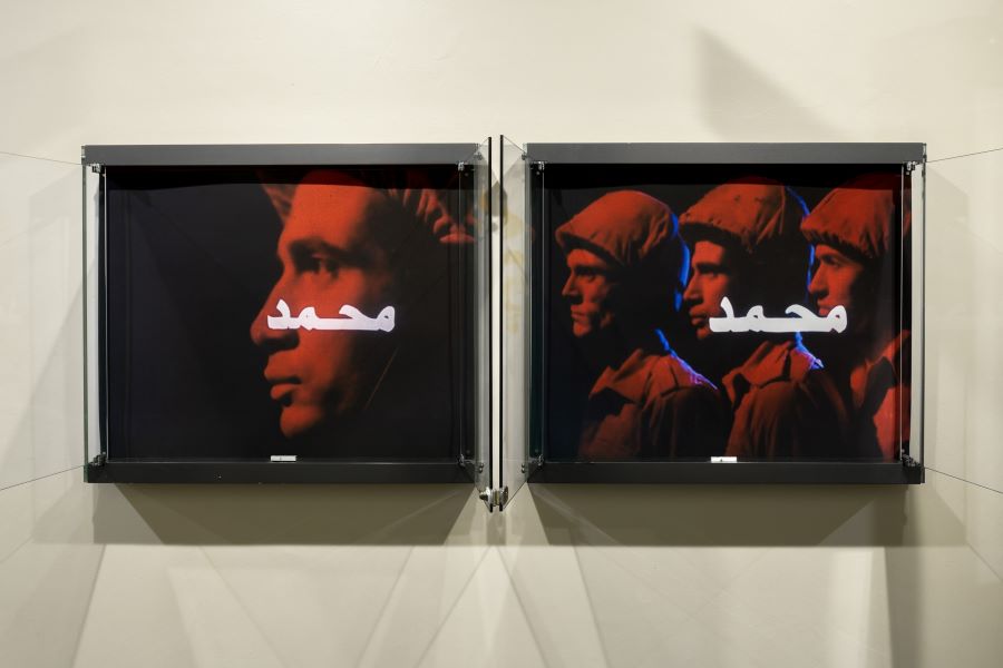 Two photographic artworks featuring soldiers illuminated in red and blue light, their space around them is black whilst Arabic text sits over their faces. 
