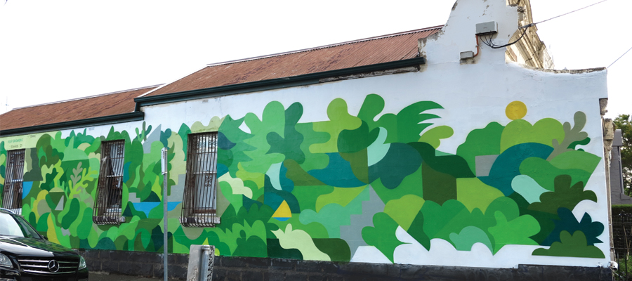 A terrace house is the canvas for a mural which uses multiple shades of green to create a vine like structure that almost encapsulates the house. 