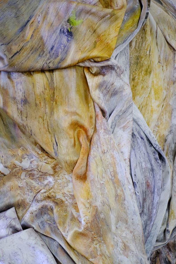 Abstract golden, lavender washed fabrics are piled within the frame