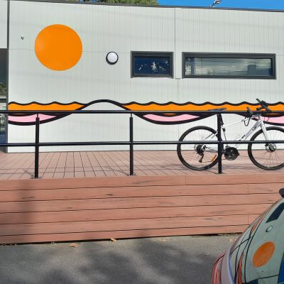 Photo of an orange wall mural displaying an abstract sun and ocean on a silver tin building. 