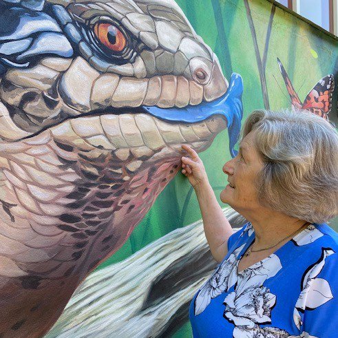 Person in a blue top touching lizard mural on the wall
