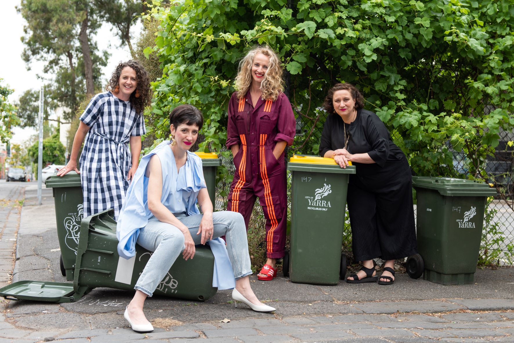 Hotham St Ladies. There are four people standing and sitting amongst a range of Yarra recycling bins. They are all smiling and looking at the camera. 