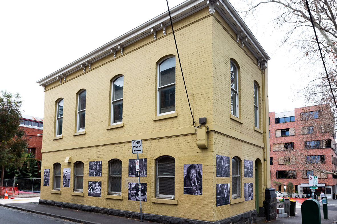 Image of the building at 12 16 Peel Street Collingwood. A brick building on a corner of Peel Street Park with posters on the walls. 