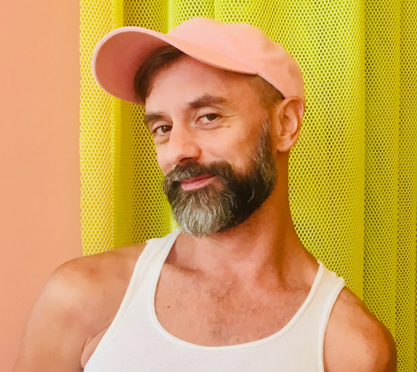 Portrait of Luke George, the artist. He wears a pink a hat, a beard and a smile. 