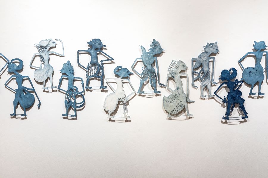 A white wall with ten blue structures of human like figures on it. The figures are multiple shades of blue, ranging from light to dark.