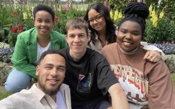 An image of SLO Collective members Kalu, Gabriel, Ranima, Mimo and Ivy. They are sitting in a garden smiling at the camera with a blue sky over head. 