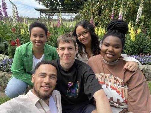 An image of SLO Collective members Kalu, Gabriel, Ranima, Mimo and Ivy. They are sitting in a garden smiling at the camera with a blue sky over head. 