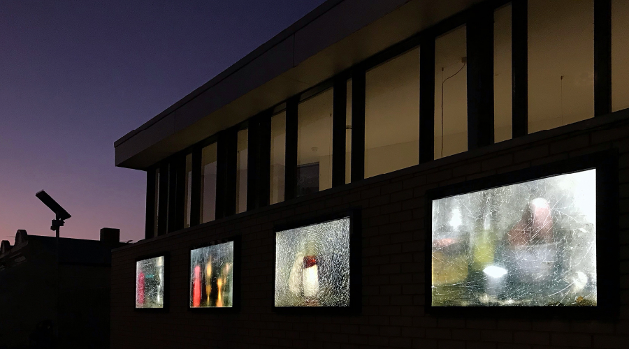 Four lightboxes illuminated under the windows of Carlton Library. Behind the building is a gradient at dusk.