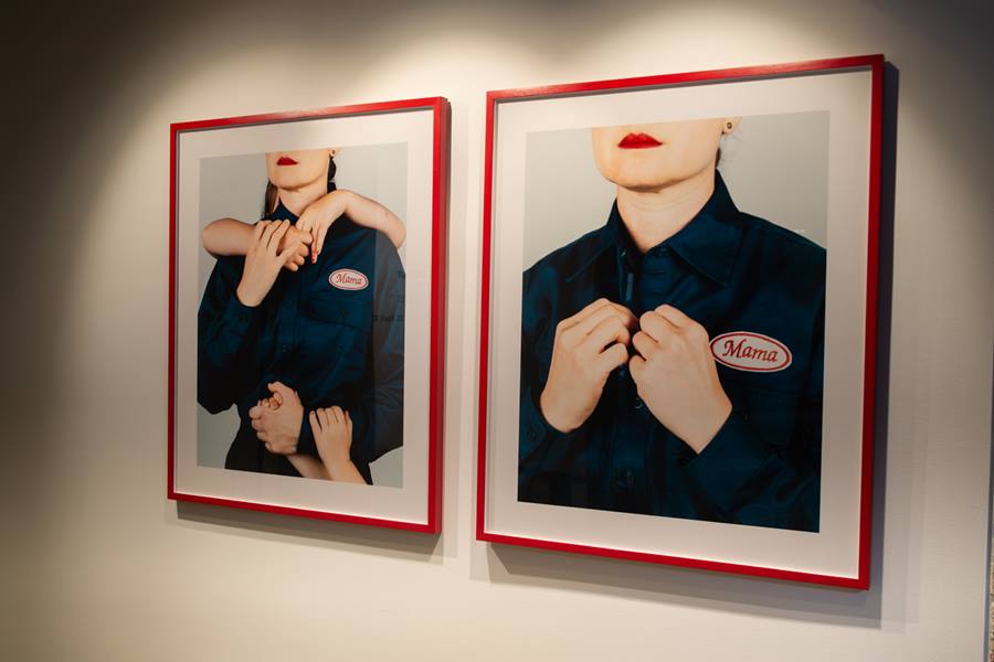 Two digital pictures with red frames side by side on a white wall. The pictures contain two people wearing overalls with the emblem 'mama'.