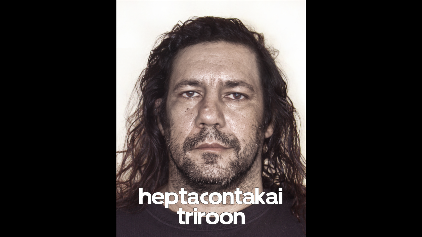 An image of a person with a neutral expression with a beard and long dark hair with "heptacontakai triroon" written in white text over the image. 