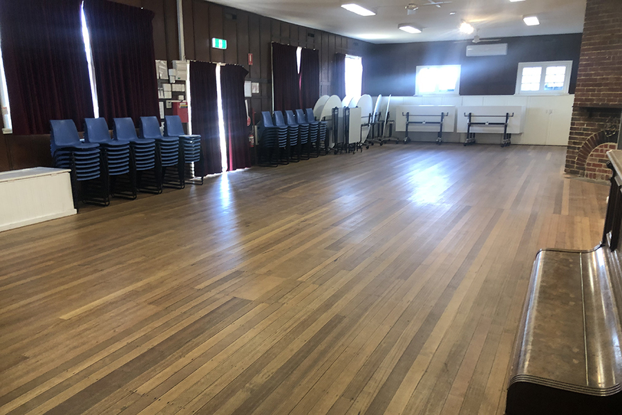 A community hall with a wooden floor and furniture lined up around the edge of the room