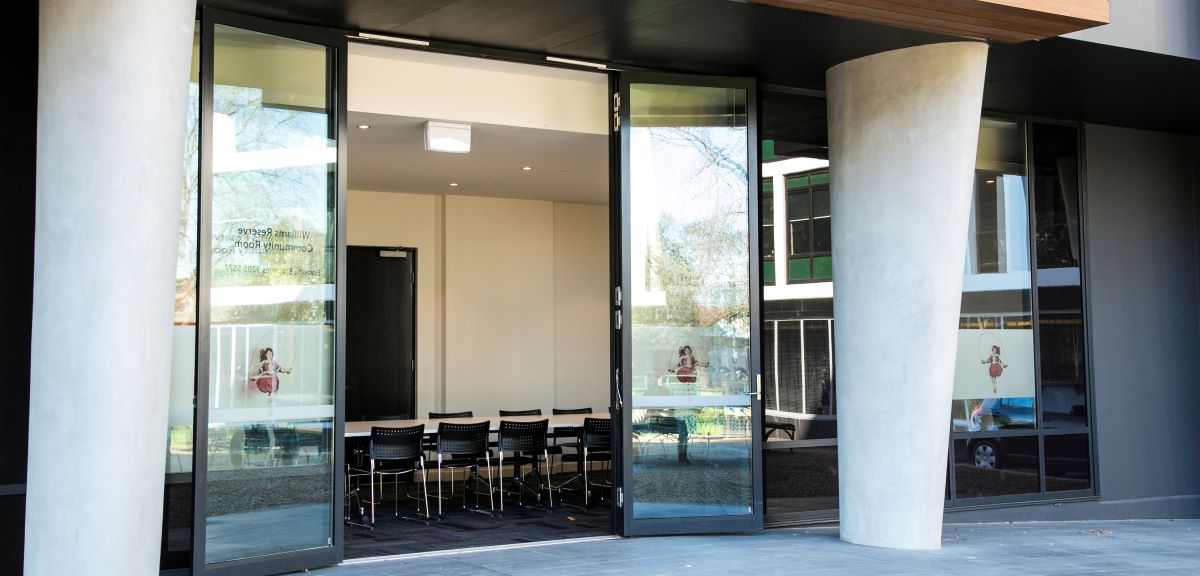 An image of the external doors of Williams Reserve. A modern building with large glass doors and tables and chairs inside.