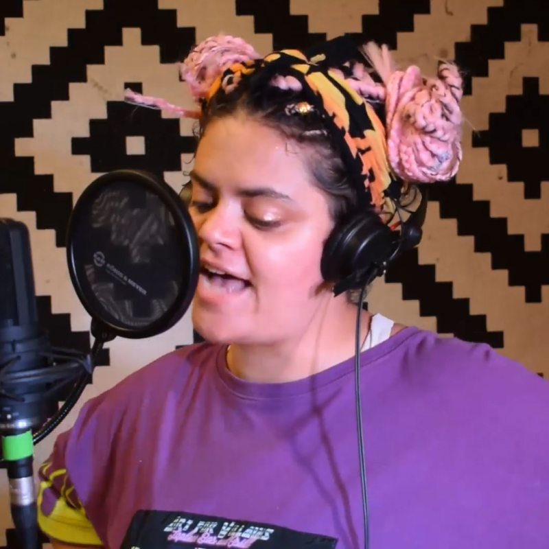 Artist Racerage wearing a purple tshirt and singing in to a studio microphone