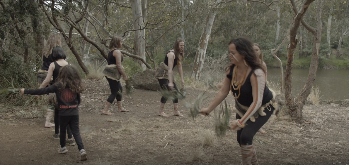 A group of Wurundjeri women in traditional dress dancing by the Yarra River