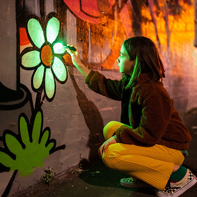 Teenager painting a flower mural on a wall with glow in the dark green paint.