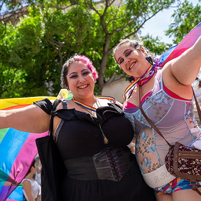 Two women waving rainbow flags at Pride Street Party