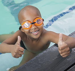 Young boy with two thumbs up sitting in the pool